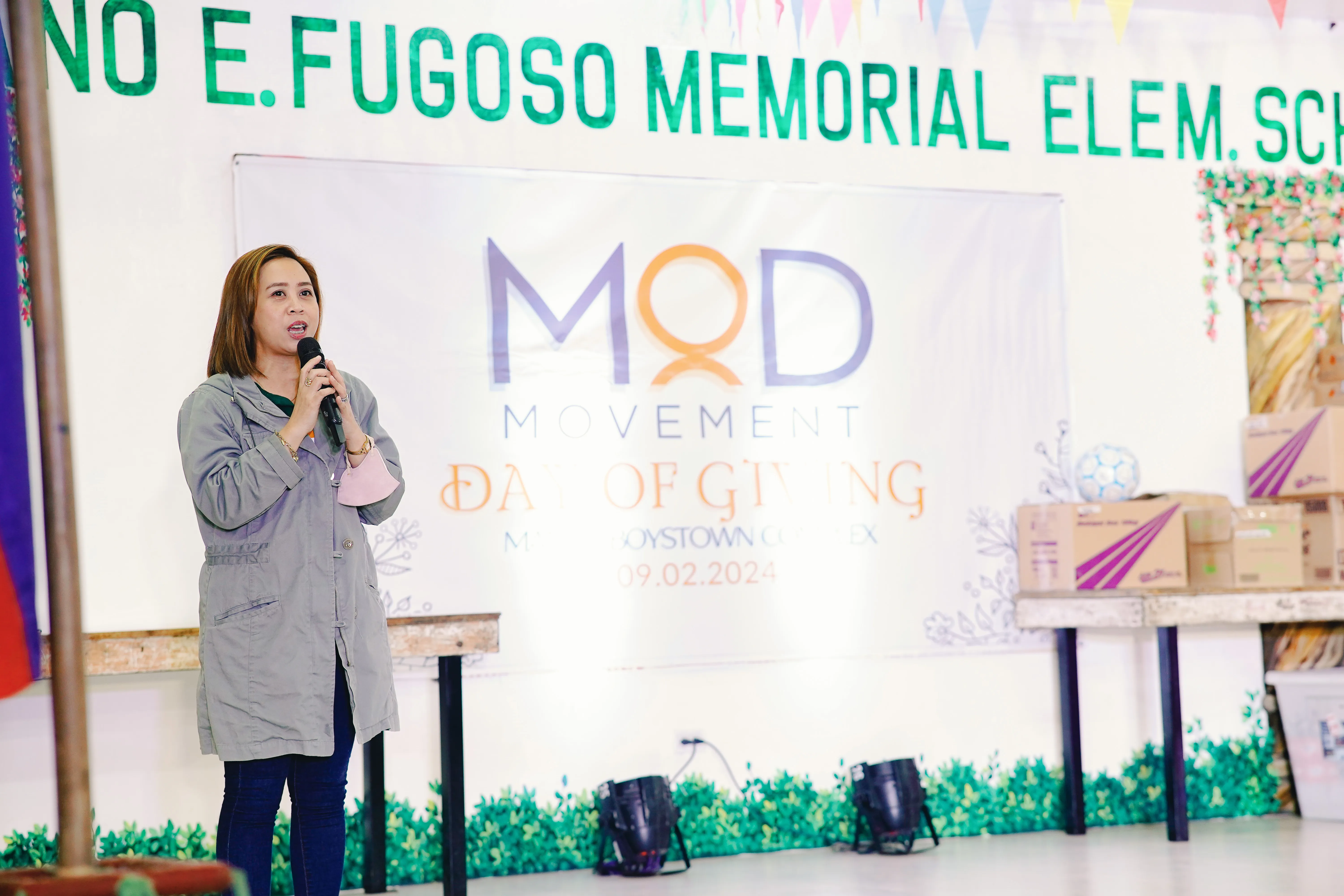 A young woman volunteer giving a speech in front of a large MOD Movement sign.